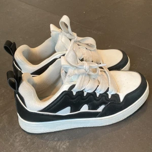 Svartvita sneakers - Snygga svartvita sneakers med breda snören och en bekväm passform. Skorna har en stilren design med svart kontrastdetalj runtom och vit sula. Perfekta för en casual look.