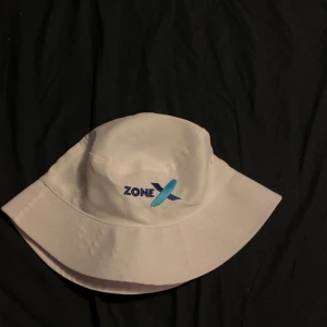 Vit hatt med Zone X-broderi - Snygg vit hatt med broderad Zone X-logga i blått och svart. Perfekt för soliga dagar och en stilren look.