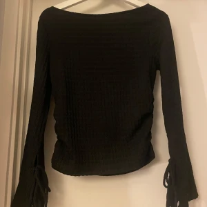Svart långärmad topp med fina detaljer - Snygg svart långärmad topp med knyt vid ärmsluten. Toppen har en texturerad yta som ger en unik look. Perfekt skick!