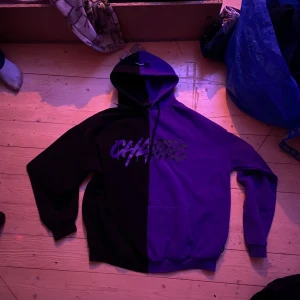 Svart och lila hoodie från Black Squad - Säljer en cool svart och lila hoodie från Black Squad med texten 'CHAOTIC' på framsidan. Hoodien har en stor ficka framtill och en bekväm passform. Perfekt för en avslappnad stil.