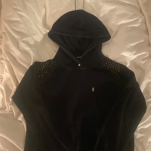 Svart hoodie från Juicy Couture - Snygg svart hoodie från Juicy Couture med gulddetaljer på axlarna och en liten logga framtill. Storlek s men ser större ut på bild