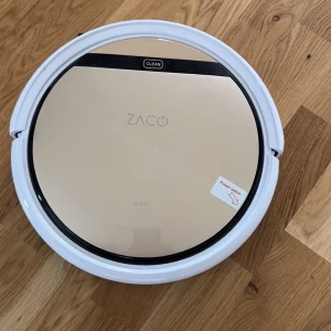 Robotdammsugare ZACO V5s Pro - Säljer en ZACO V5s Pro robotdammsugare. Den har en elegant design med vit och guld färg. Perfekt för att hålla golven rena utan ansträngning. Inkluderar funktioner som automatisk laddning, golvmoppfunktion och olika rengöringslägen. 