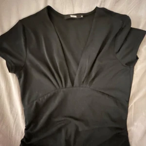 Svart topp från Bik Bok - Snygg svart topp från Bik Bok med v-ringad design. Perfekt för en stilren look. Topp har korta ärmar och en figurnära passform.