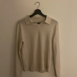 Beige tröja från These Glory Days - Säljer en stilren beige tröja från These Glory Days i Superior Merino. Tröjan har en klassisk krage och långa ärmar, perfekt för en elegant look. Materialet är mjukt och bekvämt, vilket gör den idealisk för både vardag och mer uppklädda tillfällen.