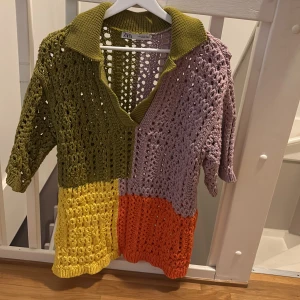 Flerfärgad stickad tröja från Zara - Säljer en unik flerfärgad stickad tröja från Zara. Tröjan har en kombination av grönt, lila, gult och orange i ett öppet stickat mönster. Den har en krage och trekvartsärmar, perfekt för att sticka ut i mängden.