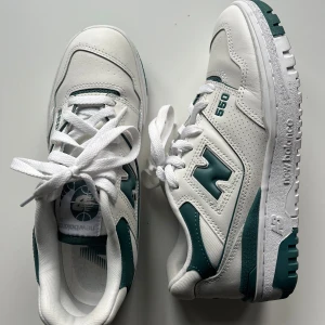 Vita och gröna sneakers från New Balance - Snygga vita sneakers med gröna detaljer från New Balance. Modellen är 550 med klassisk snörning och en sportig look. Nästan helt oanvända.