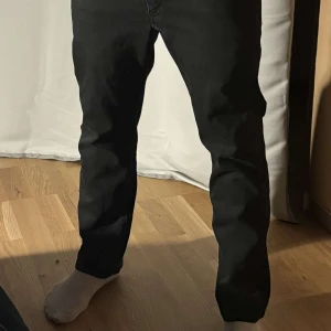 Svarta jeansbyxor från Levi's - Snygga svarta jeansbyxor från Levi's 501 med klassisk design. De har en rak passform och är perfekta för en stilren look. Byxorna har fem fickor och en knappgylf. 