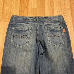 Lågmidjade bootcut jeans med specialfickor  - (28) Ljusblåa lågmidjade bootcut jeans med massa fina broderade detaljer på fickor och framsida,  jeansen har snygga slitningar på låren. Midjemått rakt över: 37cm, innerbenslängd: 81 cm. Materialet är stretchigt!❤️