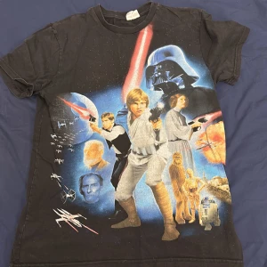 Vintage Star Wars t-shirt - Cool svart t-shirt med Star Wars-motiv. Framsidan pryds av ikoniska karaktärer och rymdskepp i färgglada tryck. Perfekt för fans av serien! Baksidan har en liten Star Wars-logga i gult.
