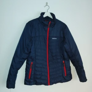 Mörkblå pufferjacka från Marine - Säljer en mörkblå pufferjacka från Marine med röda detaljer. Jackan har en dragkedja framtill och två fickor med dragkedjor. Perfekt för kyliga dagar med sin quiltade design.