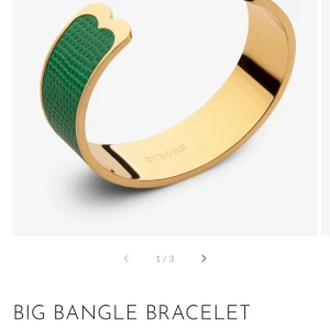 Stort armband i guld och grönt - Elegant stort armband med en guldig bas och en grön texturerad yta. Armbandet har en unik design med en vågig kant som ger det en modern touch. Perfekt för att lyfta vilken outfit som helst. Nypris - 1300kr