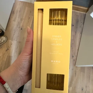 Gula middagsljus med hållare från MANO - Set med 2 gula middagsljus och hållare från MANO. Ljusen är 20 cm långa och gjorda av 100% paraffin. De brinner i upp till 7 timmar. Hållarna är av glas och mäter 5,2 x 5,7 cm. Perfekta för att skapa en mysig stämning vid middagsbordet.