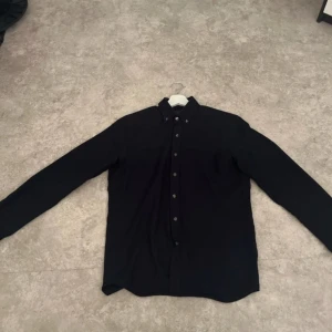 Mörkblå skjorta från Oscar Jacobson - Snygg mörkblå skjorta från Oscar Jacobson i storlek S. Skjortan har långa ärmar och knappar framtill samt vid kragen. Perfekt för en stilren look.