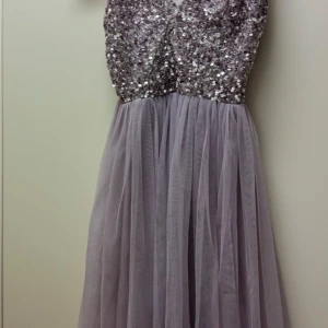 Ljuslila paljettklänning - Säljer en fantastisk ljuslila långklänning med glittrig paljettöverdel och v-ringning. Kjolen är i ett luftigt och flödande material som ger en elegant look. Perfekt för speciella tillfällen!