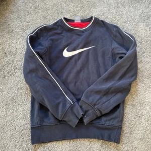Mörkblå sweatshirt från Nike - Säljer en mörkblå sweatshirt från Nike med det klassiska swoosh-loggan på bröstet. Tröjan har långa ärmar och ribbade muddar vid ärmslut och nederkant. Perfekt för en avslappnad stil.                     