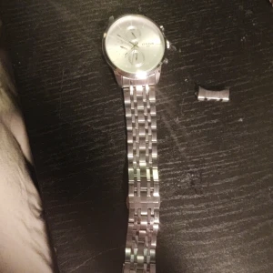 Silverfärgad klocka från Citizen - Elegant silverfärgad klocka från Citizen med en stilren urtavla och länkarmband i rostfritt stål. Klockan har en klassisk design med en rund boett och tydliga markeringar. Perfekt för den som söker en tidlös accessoar. Armbandet är av på ena sidan men inget som inte en 50 lapp kan fixa 