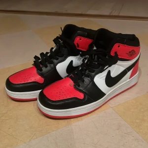 Nike i svart, röd och vit - Snygga Nike skor i en klassisk färgkombination av svart, röd och vit. Skorna har en hög modell med snörning och den ikoniska Nike-loggan på sidan. Perfekta för dig som vill ha en stilren och sportig look. Priset kan diskuteras vid snabb affär