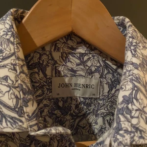 Blommig skjorta från John Henric - Snygg blommig skjorta från John Henric i 100% bomull. Skjortan har ett detaljerat blommönster i blått och vitt, perfekt för en snygg outfit! Skicket är 10/10. 