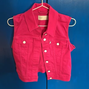 Rosa jeansväst med knappar från Levis - Säljer en cool rosa jeansväst med vita knappar. Västen har en klassisk krage och två bröstfickor med lock. Snygg färg till sommaren, aldrig använt🩷