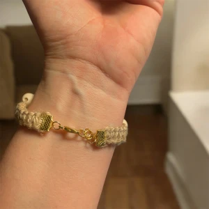 Beige armband med träpärlor - Charmigt beige armband knuten med makramé med jutesnöre och träpärlor i två storlekar. Armbandet har guldfärgade metalldetaljer och en enkel krokstängning. Perfekt för en naturlig och bohemisk stil.