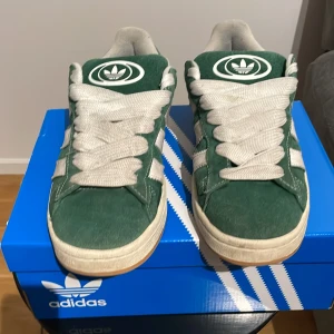 Gröna Adidas sneakers - Snygga gröna Adidas sneakers med vita detaljer och snörning. Skorna har en klassisk design med Adidas-loggan på tungan och hälen. Sulan är i gummi och ger bra grepp. Perfekta för en avslappnad stil.