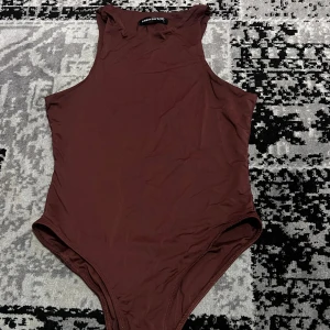Brun ärmlös bodysuit  - Snygg brun ärmlös bodysuit. Perfekt för lager-på-lager eller att bära som den är. Den har en enkel och stilren design som passar till många olika outfits. Helt ny!