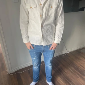 Vit overshirt med knappar - Snygg vit overshirt med knappar framtill och två bröstfickor. Perfekt för lager-på-lager-stilen. Passar bra till jeans för en avslappnad look. Modellen är 188cm 82kg. Storlek S sitter som M