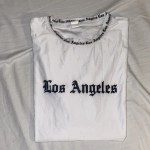 Vit Los Angeles t-shirt med tryck - Vit t-shirt med svart Los Angeles-tryck på bröstet och textdetaljer runt halsringning och ärmslut. Klassisk passform och rund hals. Perfekt för dig som gillar streetstyle och enkel design.