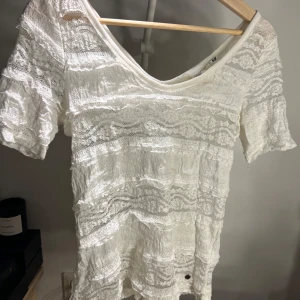 Vit spetsblus från H&M L.O.G.G. - Superfin vit blus från H&M L.O.G.G. med v-ringning och korta ärmar. Blusen har ett romantiskt spetsmönster i hela tyget och är tillverkad i ett lätt, luftigt material. Perfekt för dig som gillar en feminin och bohemisk stil.