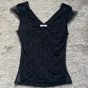 Svart blus Vila - Supersnygg svart blus från Vila med v-ringning och transparent mesh. Vissa pärlor har ramlat av (se bild).