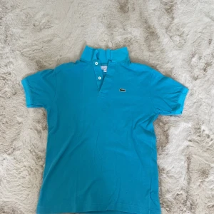 Turkos pikétröja från Lacoste - Snygg turkos pikétröja från Lacoste med klassisk krage och två knappar framtill. Ikoniska krokodilloggan broderad på bröstet. Gammal så vet inte om dem har mer värde pris kan diskuteras💕💕