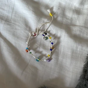 Färgglatt pärlarmband med snörning - Ett handgjort armband med vit snodd och massor av färgglada pärlor i olika former och nyanser. Armbandet har justerbar knytning och ger en lekfull och personlig touch till din stil.