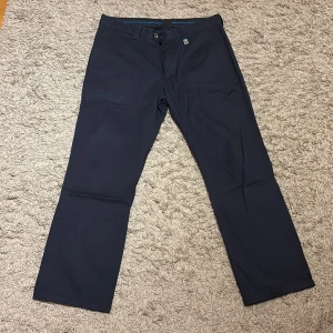 Mörkblå golfbyxor från Cross - Snygga mörkblå golfbyxor från Cross Sweden i klassisk rak modell. Byxorna har hällor för bälte, två fickor fram och två bakfickor. Perfekta för en clean och stilren look. Materialet känns mjukt och följsamt. Användes till golf.