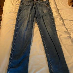 Replay Anbass ljusblå jeans slim fit - Säljer ett par snygga ljusblå Replay Anbass jeans i slim fit. Jeansen har klassisk femficksdesign, dragkedjegylf och diskreta slitningar för en cool look. Perfekta för dig som gillar en smalare passform och stilren denim.