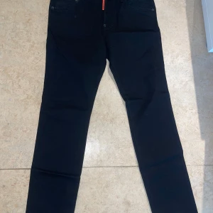 Svarta jeans från Dsquared2 - Snygga svarta jeans från Dsquared2 med klassisk femficksdesign och coolt patch med orange Dsquared2-logga bak. Jeansen har smal passform och raka ben, perfekta till sneakers eller boots. Materialet är mjukt och stretchigt för extra komfort.