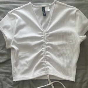 Vit ribbad croppad topp  - Snygg vit croppad topp från HM med ribbad struktur och v-ringning. Toppen har korta ärmar och snörning framtill. Ny skick!