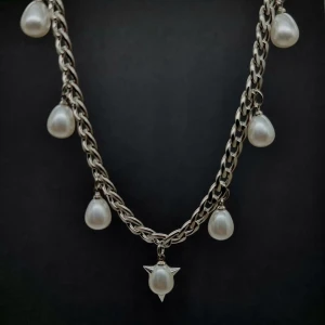 Chunky halsband med pärldroppar - Stilrent halsband i silverfärgad metall med sju hängande droppformade pärlor, varav en har coola stjärndetaljer. Kedjan är chunky och ger ett edgy intryck, perfekt för att lyfta vilken outfit som helst. Pärlorna är vita och ger en snygg kontrast mot den silvriga kedjan.