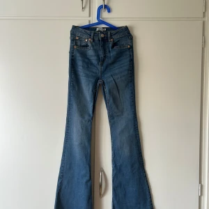 Blå flare jeans från 157 Snake Flare - Snygga blå jeans från 157 i modellen Snake Flare med klassisk femficksdesign och utsvängda ben. Jeansen har normal midja och är tillverkade i ett mjukt denimtyg med snygga slitningar. Perfekta för dig som gillar retrovibbar och vill sticka ut.