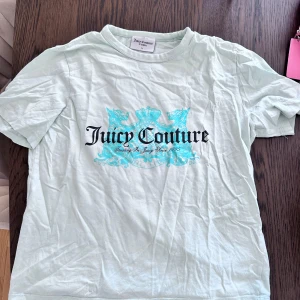 Vit Juicy Couture t-shirt - Snygg vit t-shirt från Juicy Couture med stort turkost tryck och logga framtill. Klassisk passform med rund hals och korta ärmar. Perfekt för dig som gillar statement-plagg och vill sticka ut lite extra.