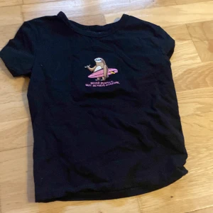 Svart t-shirt med broderad sengångare - Svart t-shirt från House i bomull med korta ärmar. På bröstet finns en broderad sengångare med en rosa surfbräda och texten 'Never perfect, but always awesome'. Perfekt för dig som gillar chill vibes och coola prints.