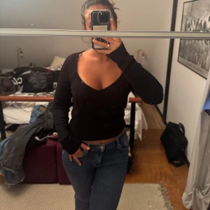 Svart ribbad tröja - Säljer en svart tröja med v-ringning och långa ärmar. Tröjan är ribbad och sitter tajt, perfekt att styla med jeans eller kjol. Enkel och stilren design som passar till många olika looks.