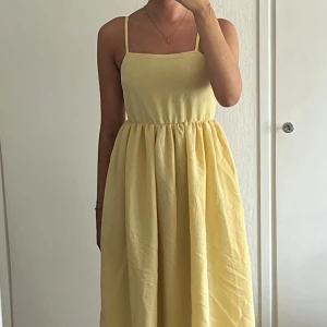 Gul sommarklänning knyte i ryggen - Ljusgul långklänning med smala axelband, öppen rygg och knytning bak. Klänningen har en rak urringning och ett lätt rynkat midjeparti som ger en flowy känsla. Perfekt för varma dagar. Finns några fläckar efter att den legat i garderoben ett tag men går säkert bort i tvätten (se bilder). Köpt på Nelly. 