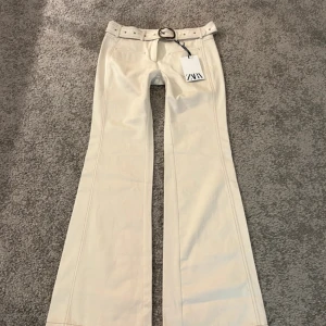 Jeans med bälte från Zara - Snygga creme vita jeans från Zara med tillhörande bälte och coolt spänne. Byxorna har låg midja, raka sömmar och är tillverkade i ett mjukt bomullsmaterial. Perfekta för dig som gillar en trendig och stilren look. Oanvändaed lappen kvar. Limited edition. 