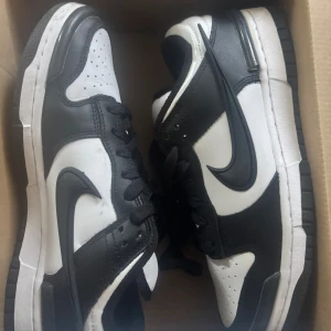 Nike Dunk Low svartvita sneakers - Säljer ett par Nike Dunk Low sneakers i svart och vitt skinn med klassisk Swoosh-logga på sidorna. Skorna har snörning, platt sula och rund tå. Perfekta för dig som gillar streetstyle och vill ha en ikonisk look.