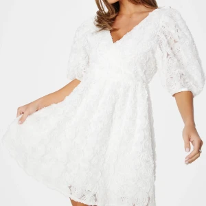 Vit blommig kortklänning med puffärm - Superfin vit kortklänning med 3D-blommor över hela tyget, v-ringning och puffiga halvlånga ärmar. Perfekt för dig som tar studenten, Säljer då jag köpte två av samma klänning. Så den jag säljer är alltså helt oanvänd i helt nytt skick!