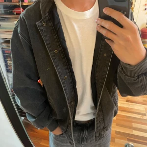 Mörkgrå jeansjacka Levi's - Säljer en mörkgrå bomberjacka från Levi's i jeansmaterial. Jackan har ribbade muddar, tryckknappar framtill och två fickor på sidorna. Oversized passform och klassisk bomberkrage ger en chill vibe. Perfekt för dig som gillar streetwear och vill ha en stilren look. Jackan är aldrig använd och har fortfarande prislapp på. Nypris 1020 kr