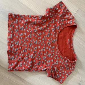 Röd blommig topp från Uniqlo - Kortärmad röd topp från Uniqlo med blåvitt blommigt mönster. Väl använd men ändå i bra skick. Färgen har tvättats av och det syns ett litet  hål. Pris kan omdiskuteras! 💗