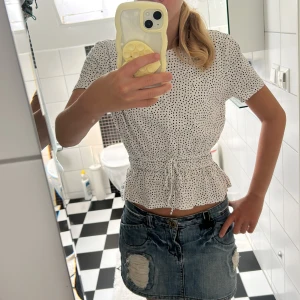 Vit prickig blus med knyt i midjan - Supersöt vit blus med svarta prickar och korta ärmar. Den har knyt i midjan och volangkant nedtill som ger en feminin och trendig look. Perfekt till jeans eller kjol för en fräsch stil. Lätt och luftig, passar perfekt till varmare dagar. Lappen är avklippt men jag skulle säga att den är mellan XS och S