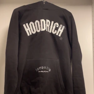 Svart Hoodie från Hoodrich med brodyr - Svart knappt använd hoodie från Hoodrich i storlek M med stor vit broderad logga på bröstet och detaljer på fickan, huvan, ryggen och armen. Klassisk känguruficka och huva, samt ribbade muddar. Perfekt för en streetwear-look. Priset är inte hugget i sten! Nypris på denna hoodien är 1100kr 