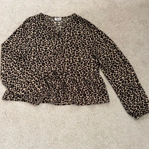 Leopardmönstrad blus från Kappahl - Snygg blus från Kappahl i leopardmönster med beige och svarta toner. Modellen har lång ärm, v-ringning,rosetter framtill och volanger.Perfekt för dig som vill sticka ut med ett djurmönstrat plagg. Materialet känns mjukt och följsamt. 🤍
